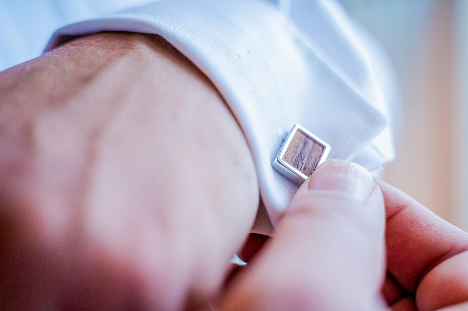 Close-up of a man adjusting his cufflinks on a white dress shirt, showcasing elegance and style.