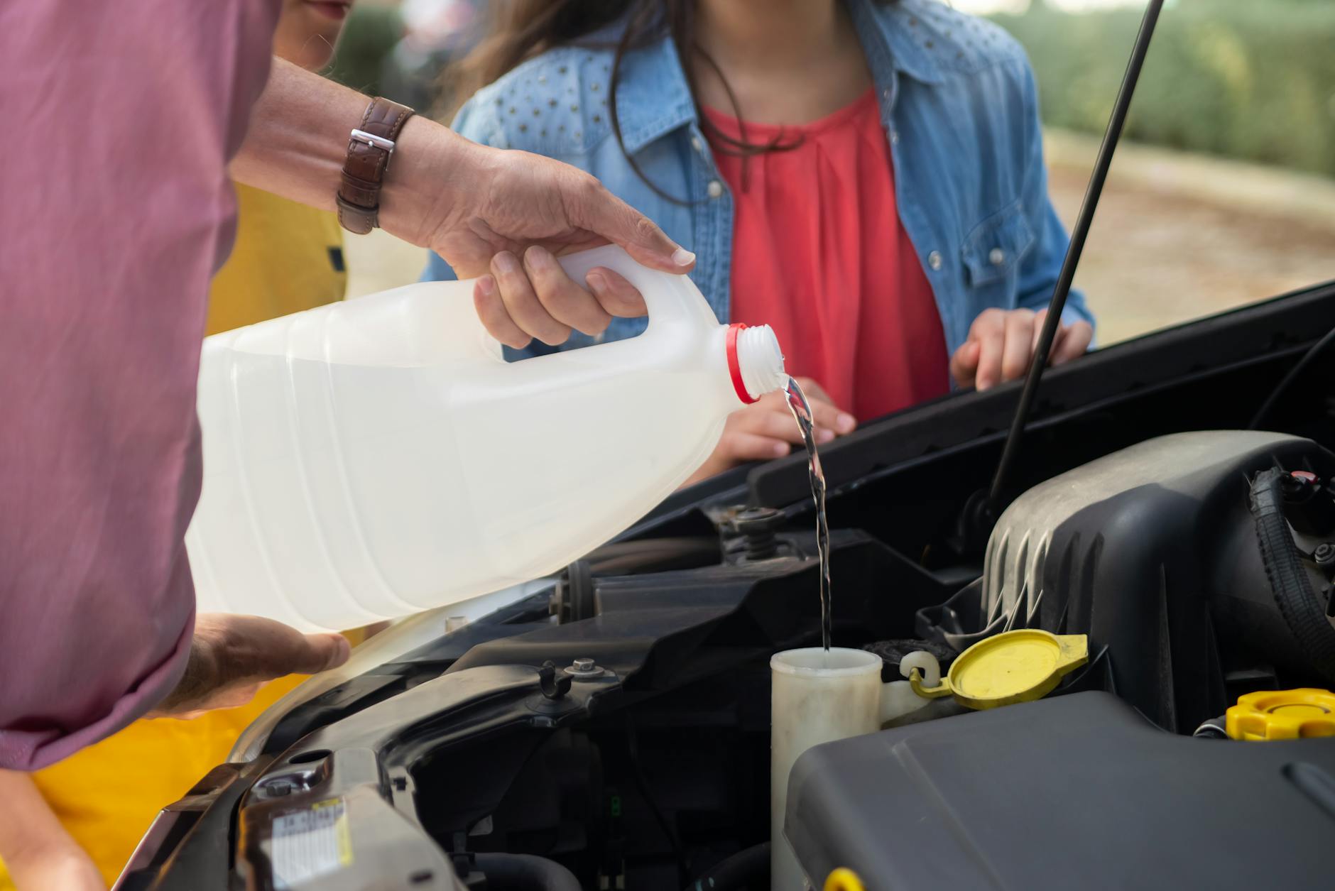 Close-up of a person pouring windshield washer fluid into a car, emphasizing vehicle maintenance.