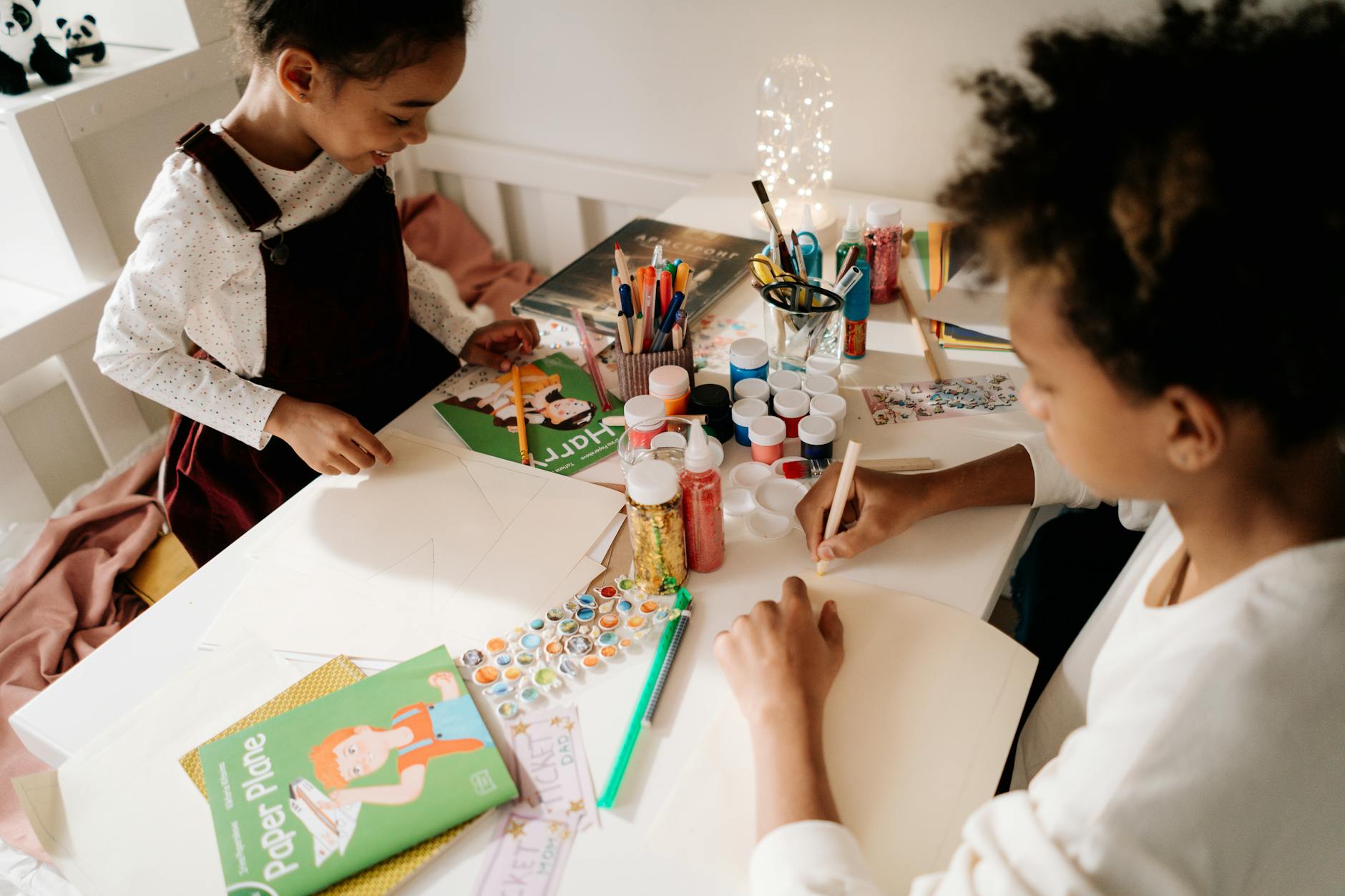 Two children enjoying arts and crafts with vibrant materials on a table indoors.