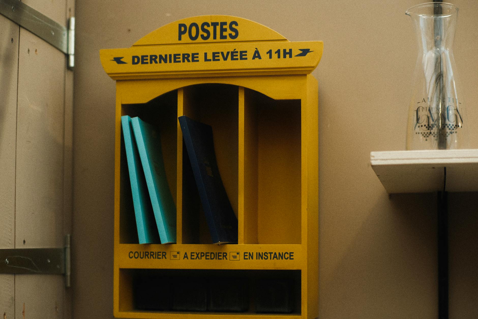 Vintage yellow postal shelf with books and a glass vase in an indoor setting.