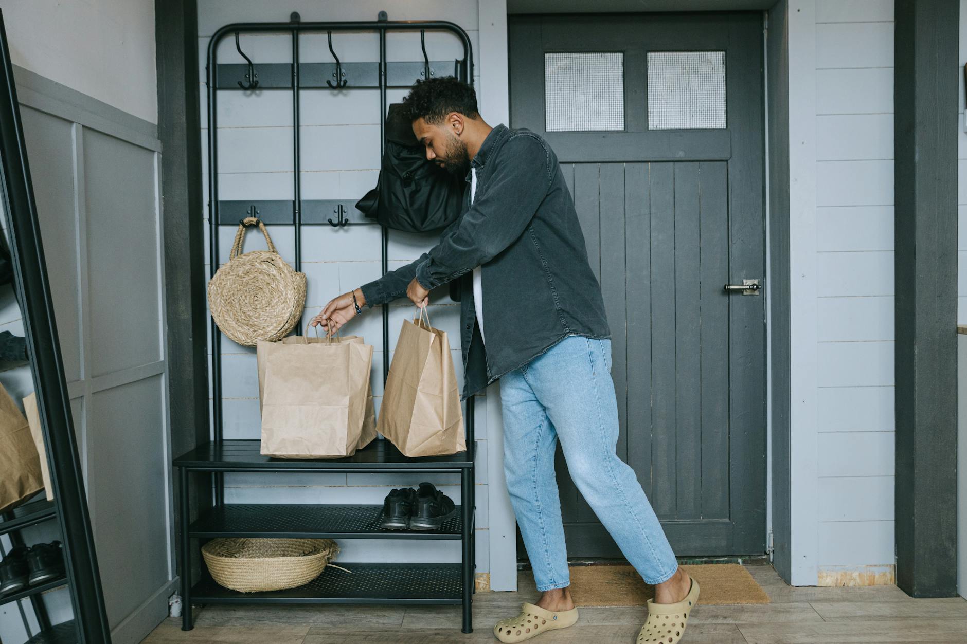 Man arranges paper shopping bags in a stylish entryway, combining fashion and home organization.