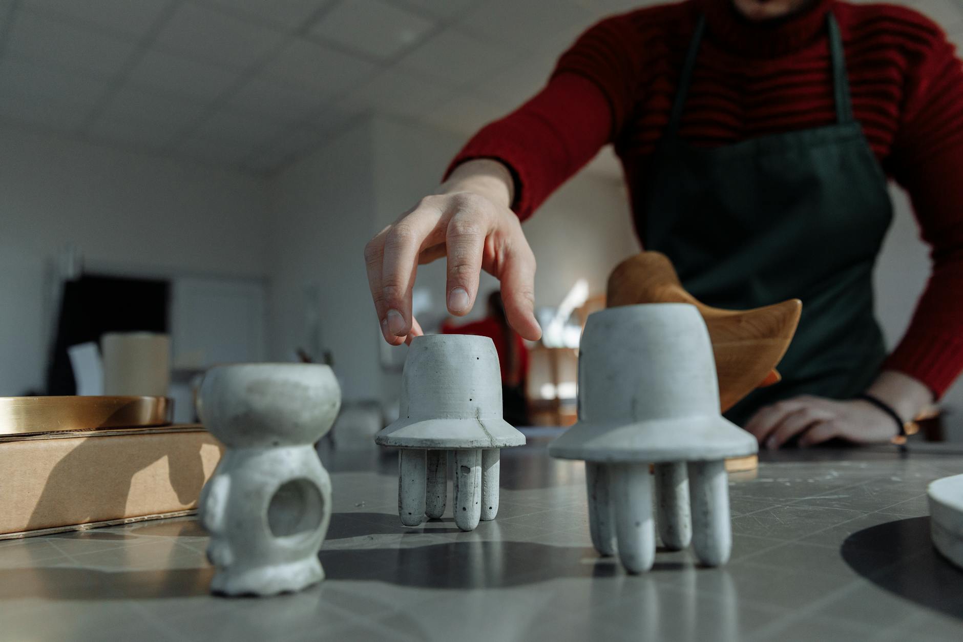 A close-up of a person sculpting unique handmade concrete figurines on a workshop table.
